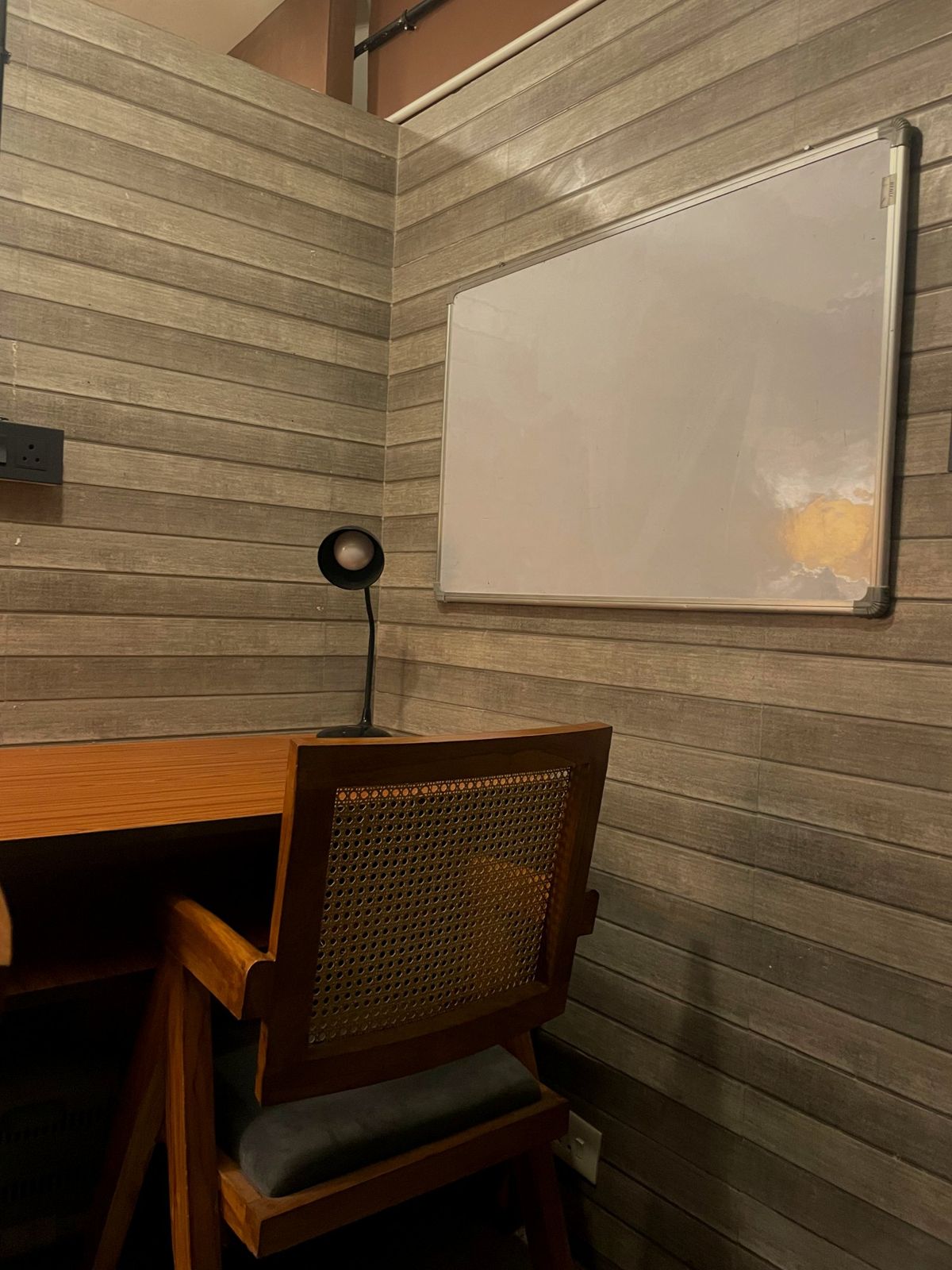 A whiteboard on the panelled wall above a desk with a lamp