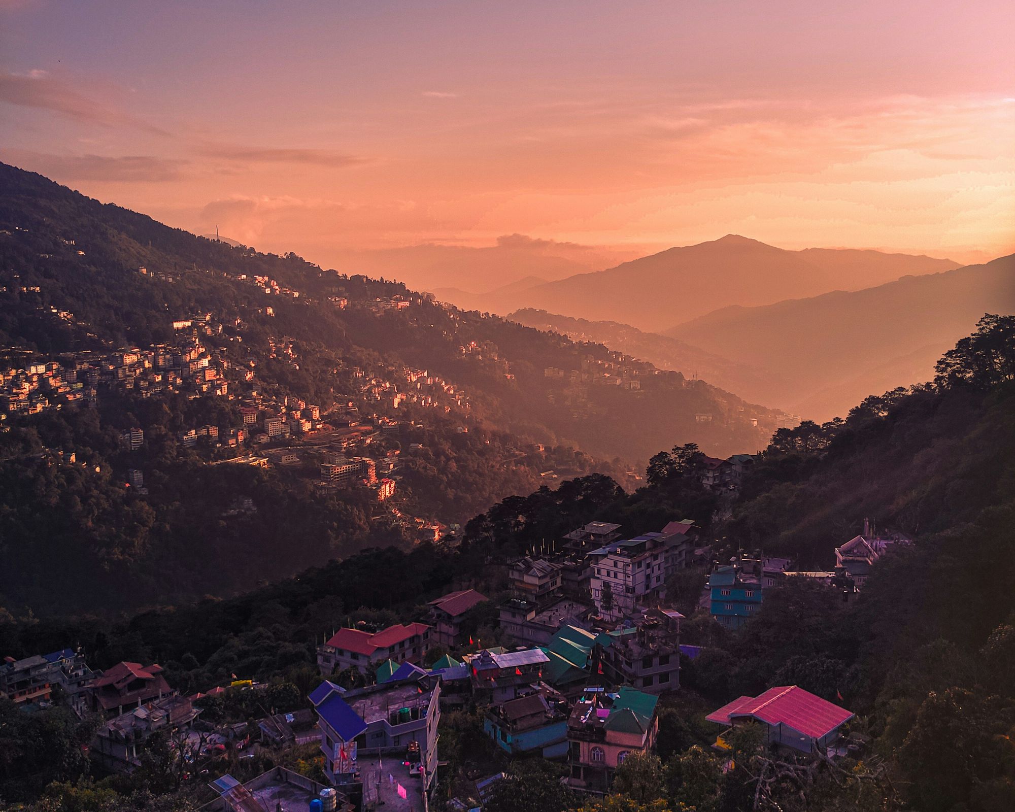 Gangtok at dusk: houses on the hillside under a pink and orange sky, with ridges fading into the distance